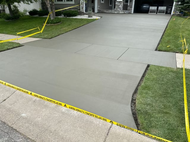 Fresh concrete driveway replacement at a suburban home, with new gray concrete, caution tape, and a car in the garage.