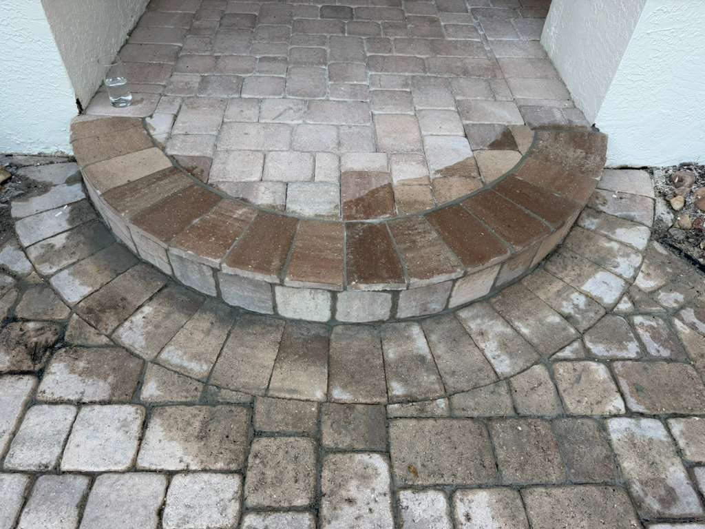 Close-up of a curved front entry step made of pavers, with stained walkway pavers below and white stucco walls on both sides.