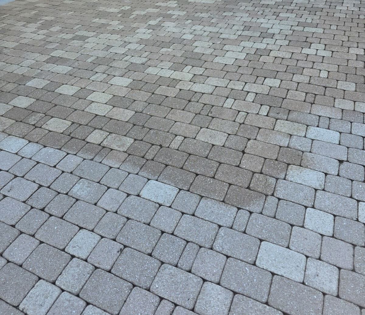 Close-up of a driveway surface made with interlocking gray and tan pavers in varied rectangular sizes. A portion of the pavers have been sealed.